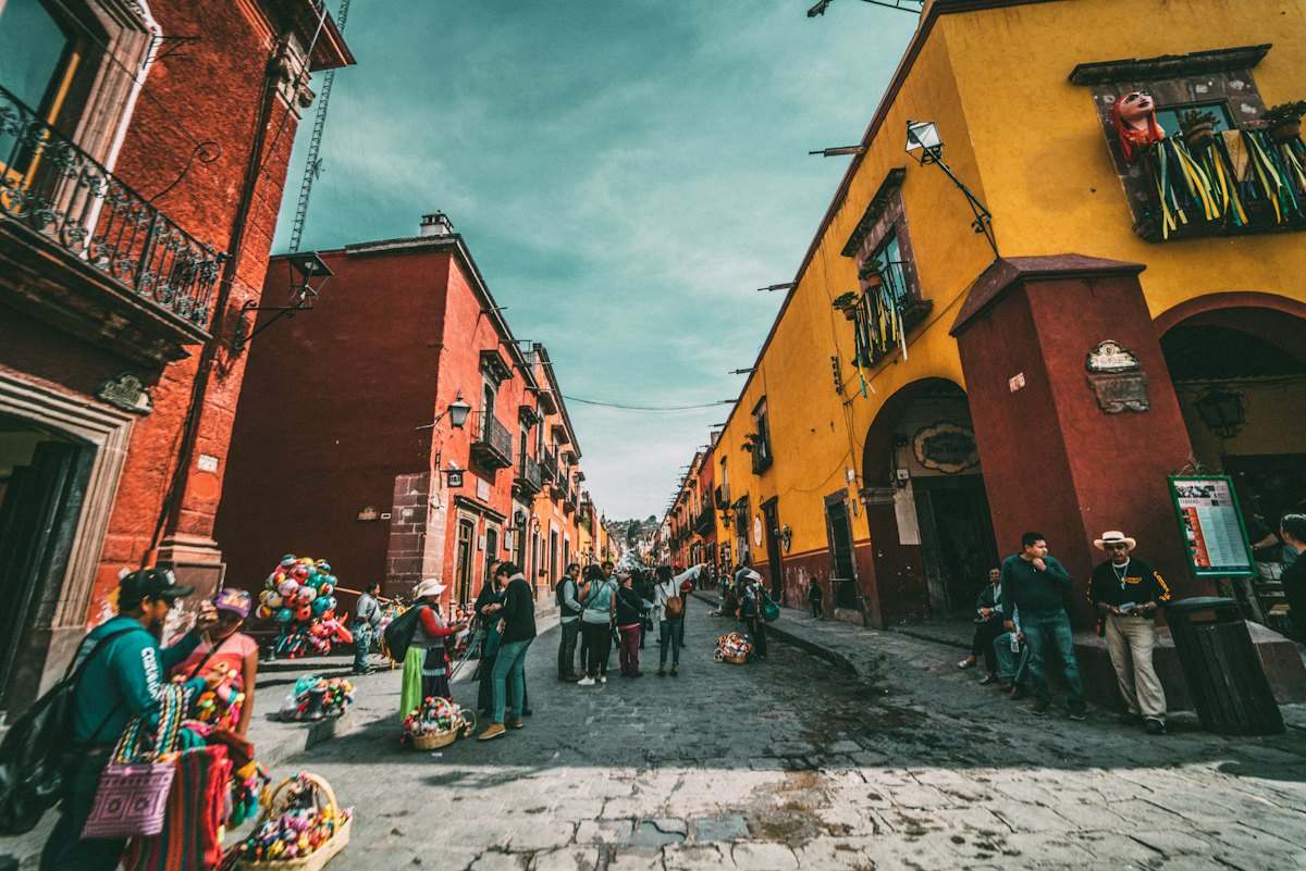Rua de pedra com casas coloridas e pessoas caminhando numa cidade do México